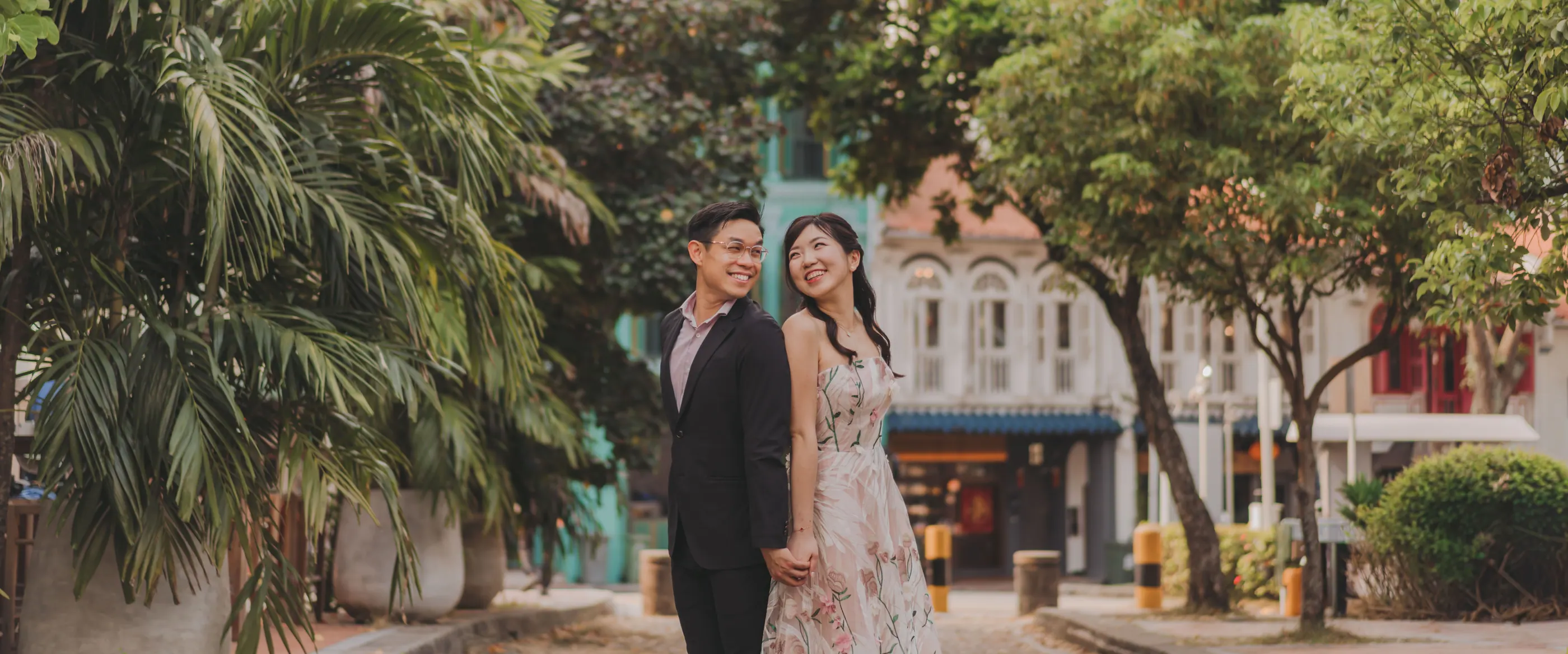 Jingwen and Thai standing together on a palm-lined street of Singapore shophouses